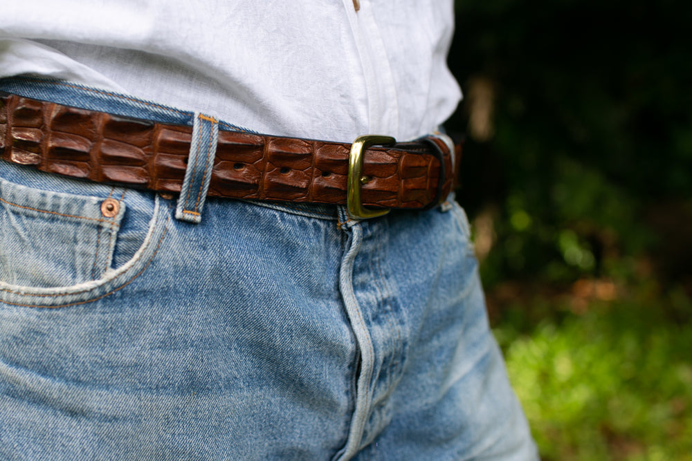 a men wearing a white linen shirt, blue jeans and a crocodile skin hornback styled belt being the focus
